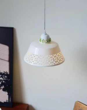 Artisanal ceramic pendant light fixture in minimalist interior corner, three-quarter angle showing green floral ceramic trim and diffused lighting