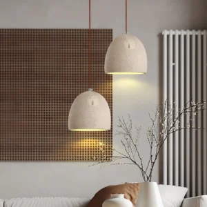 Pair of grey ceramic pendant lamps with hand-carved facial details installed in modern minimalist living room with radiator and dried flowers
