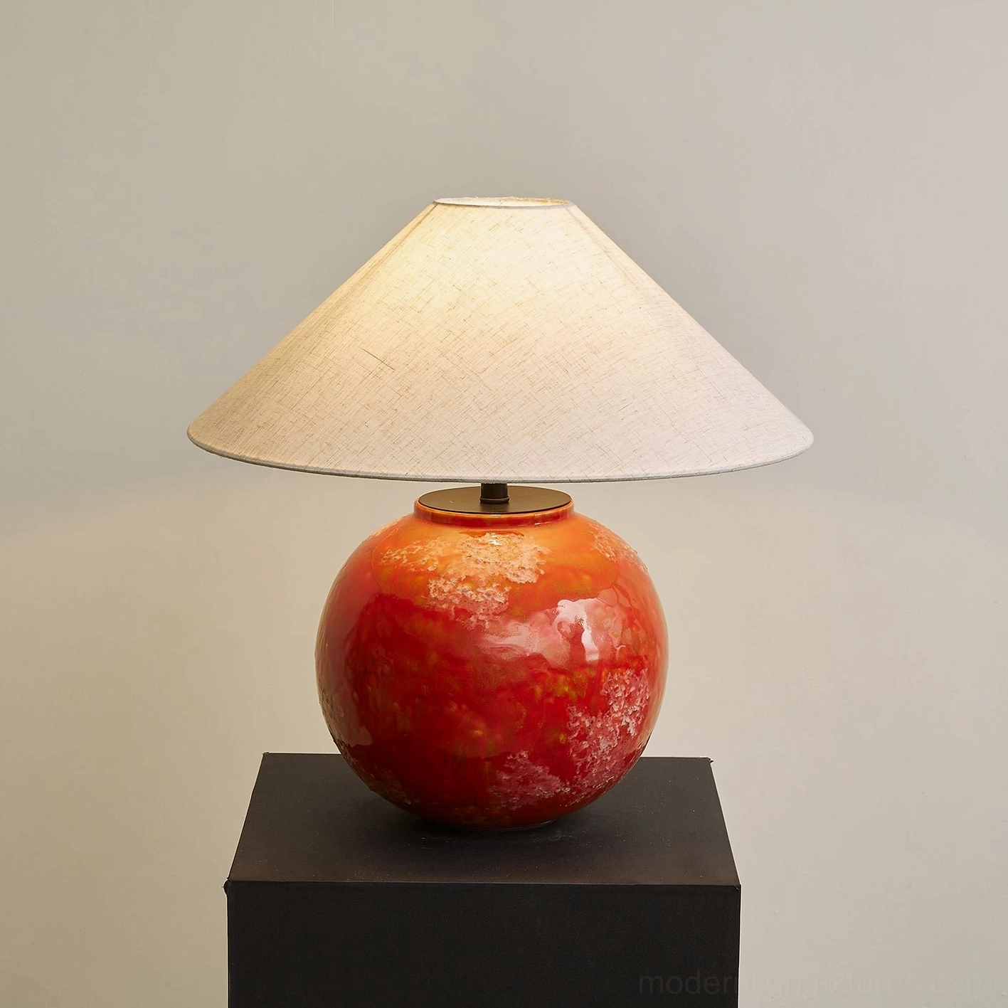 Lit contemporary red ceramic lamp with soft fabric shade glowing warmly on neutral studio platform display