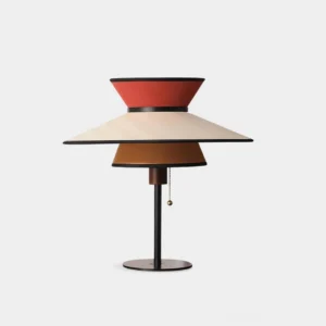 Modern conical table lamp with three-tiered layered fabric shades in warm earthy tones and orange-red accents, featuring sleek black metal stem on white studio background