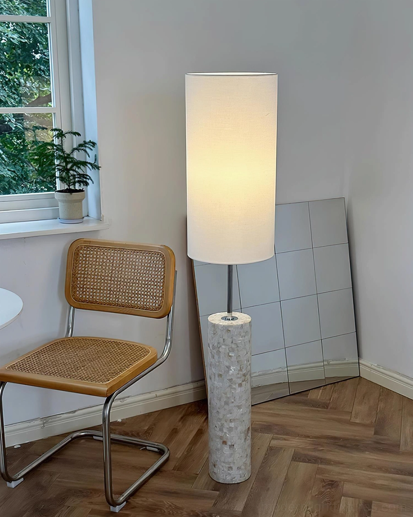 Modern cylindrical floor lamp in corner with wooden floor, window, rattan chair and potted plant