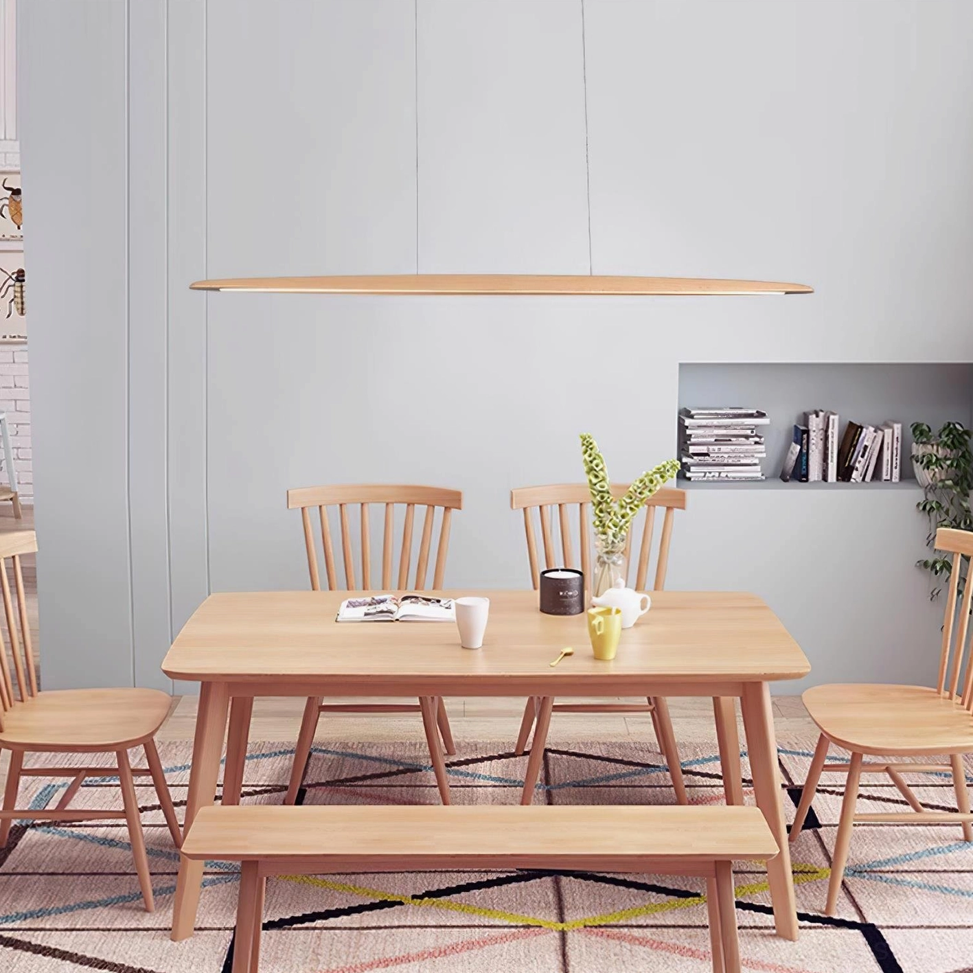 Modern dining space with linear LED pendant light natural wood finish above wooden dining set with bookshelf