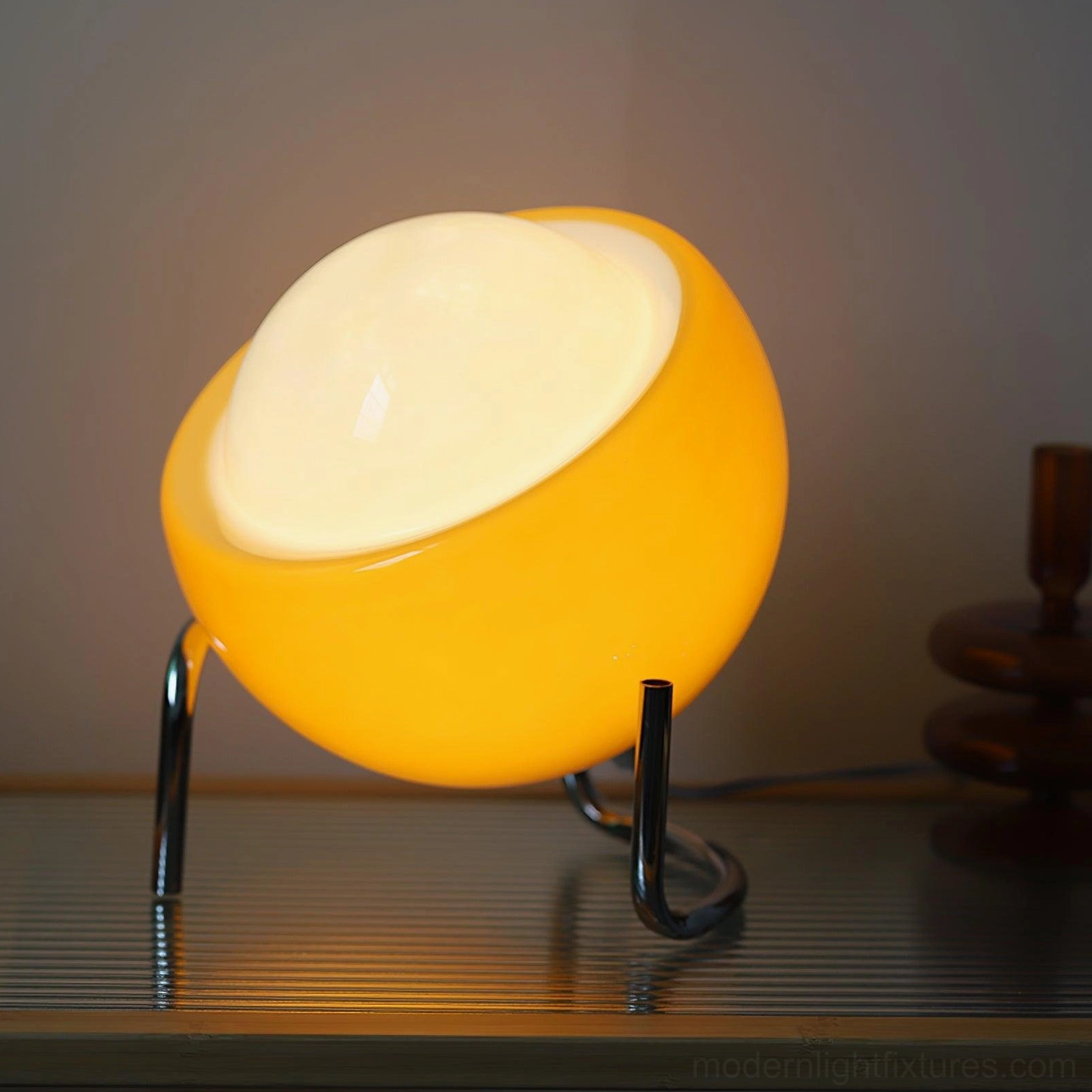 Retro tilted dome lamp with yellow glossy shade and black metal tripod stand on wooden slatted tabletop, lit