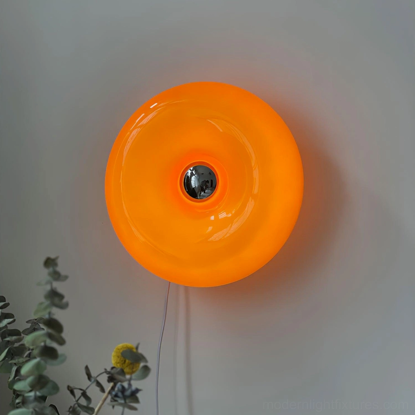 Modern donut wall sconce featuring glossy orange glass and metallic base in stylized studio photography