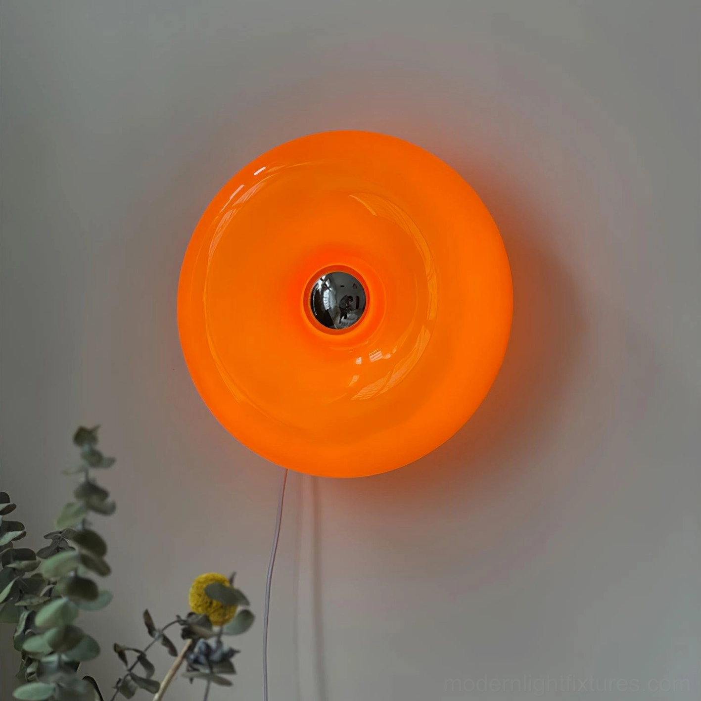 Bright orange mid-century donut wall light with central silver metal base and white hanging cord