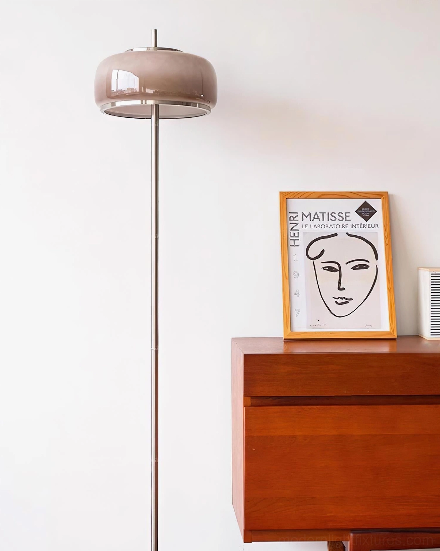 Modern mushroom floor lamp with taupe glass shade tall silver chrome pole and black base beside wooden dresser wall art