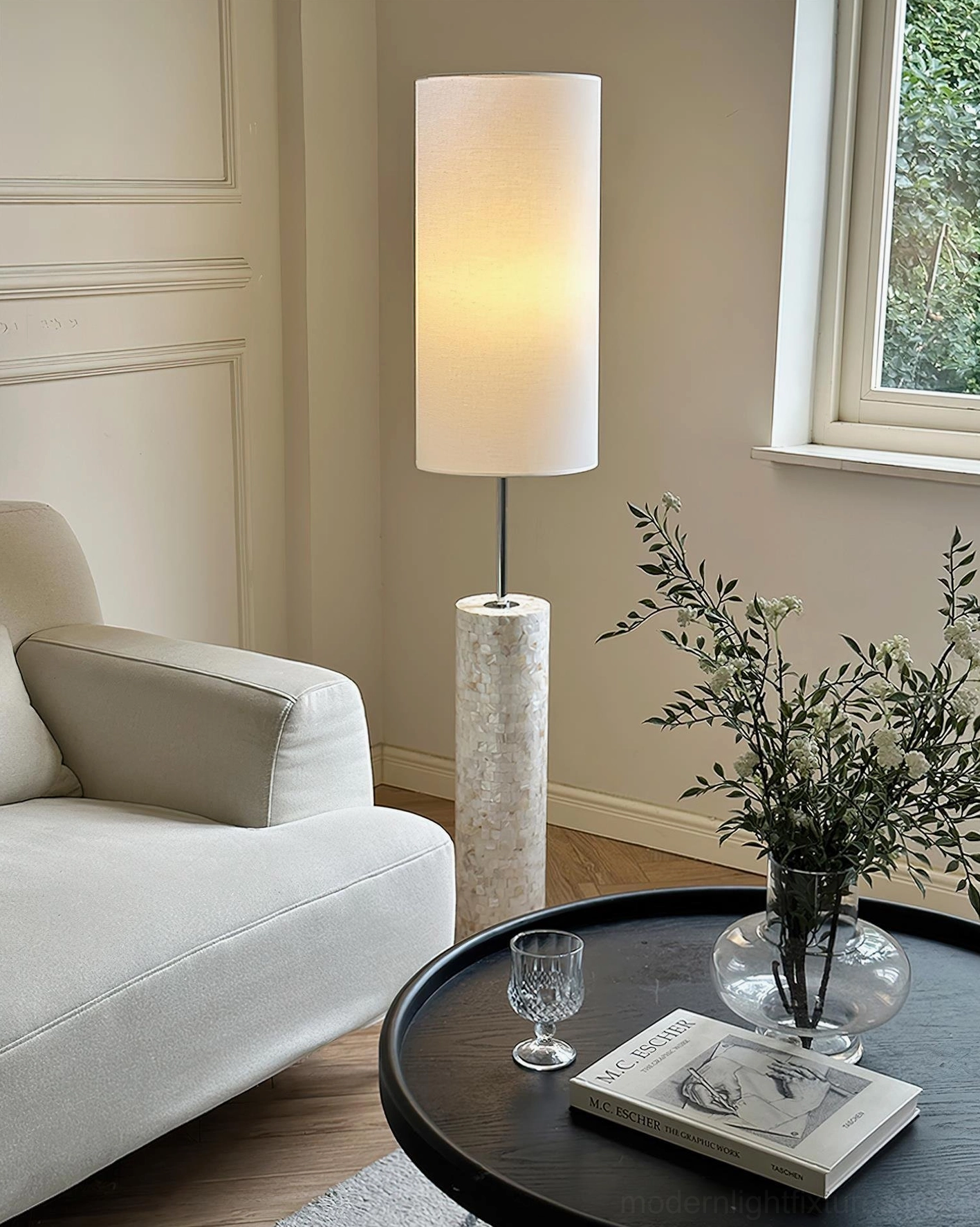 Minimalist floor lamp with warm glow beside coffee table and green potted plants in modern living room