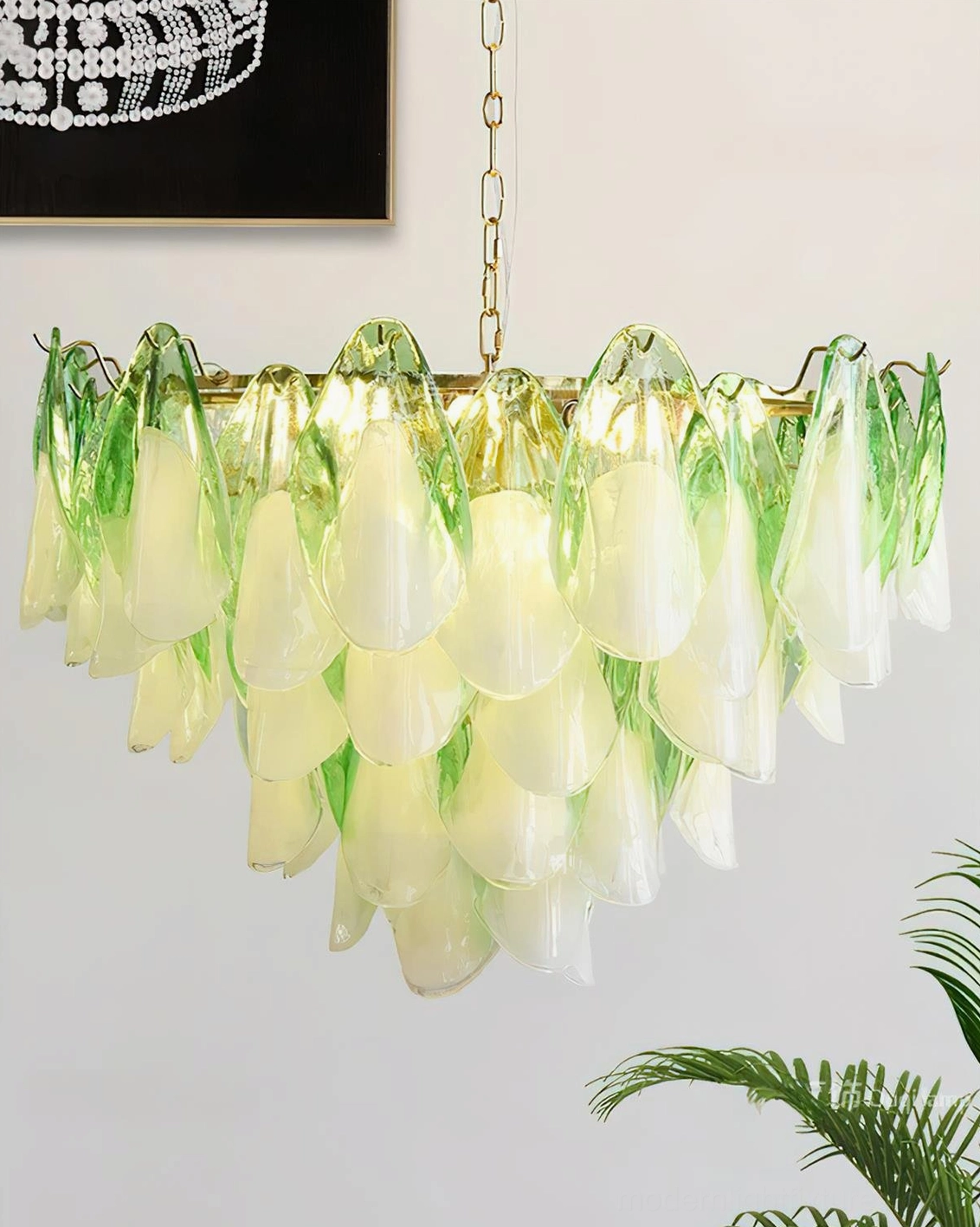 Modern handcrafted glass petal chandelier illuminated in residential dining room with warm glow and green plant decor