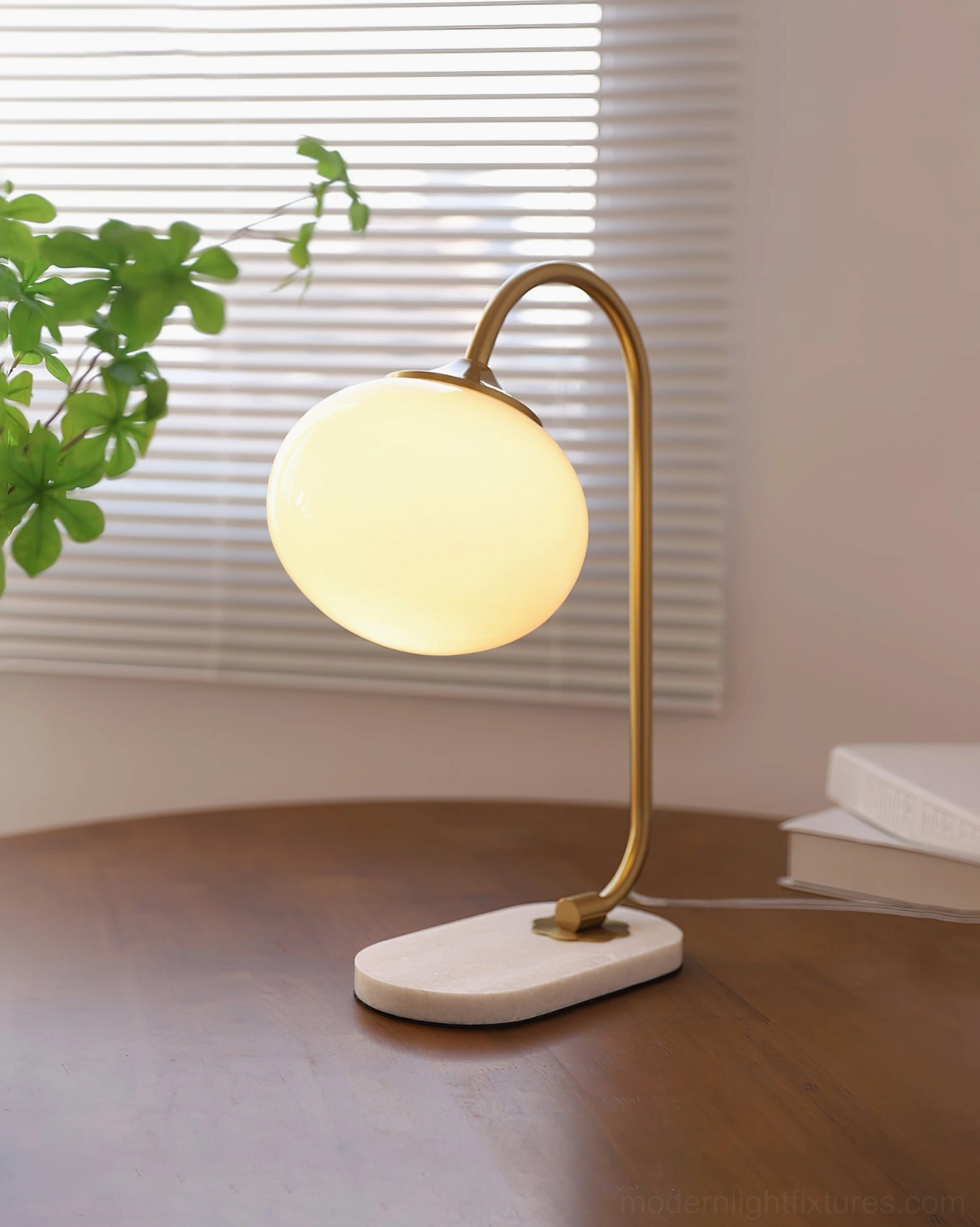Modern globe table lamp with illuminated warm glass shade, gold metal arm, and white marble base by window