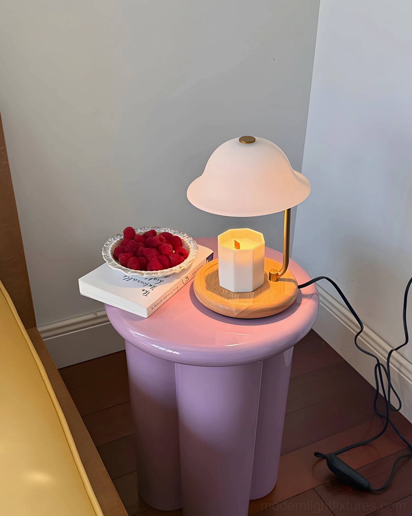 Scandinavian candle warmer lamp with lit candle on pastel purple table with book and raspberries