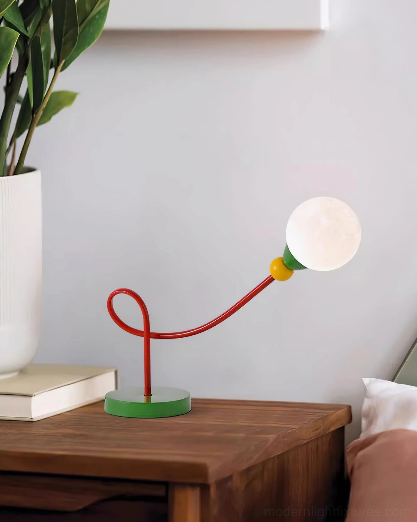 Minimalist table lamp on wooden desk with stacked books and potted plant for modern office aesthetic