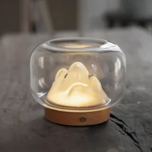 Modern warm mountain ambient lamp three-quarter view on weathered wood tabletop, soft glow highlighting grain texture