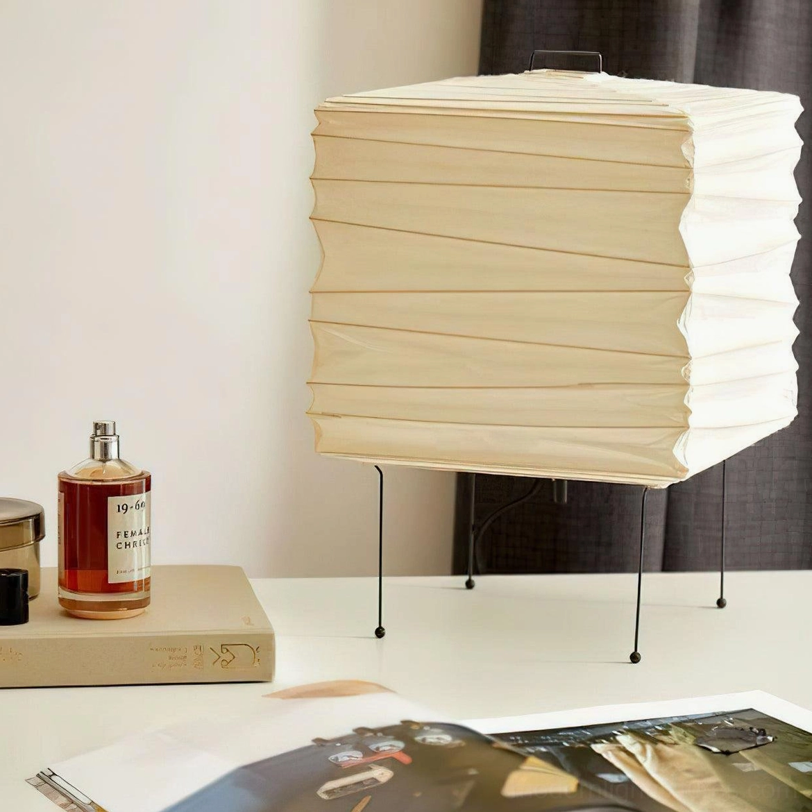 Modern paper cube lamp positioned on marble tabletop with decorative glass vases and dried branches