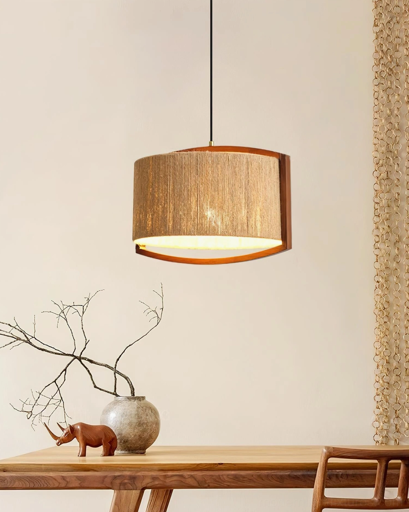 Woven jute pendant light hanging above minimalist dining table with wooden furniture and dried flowers