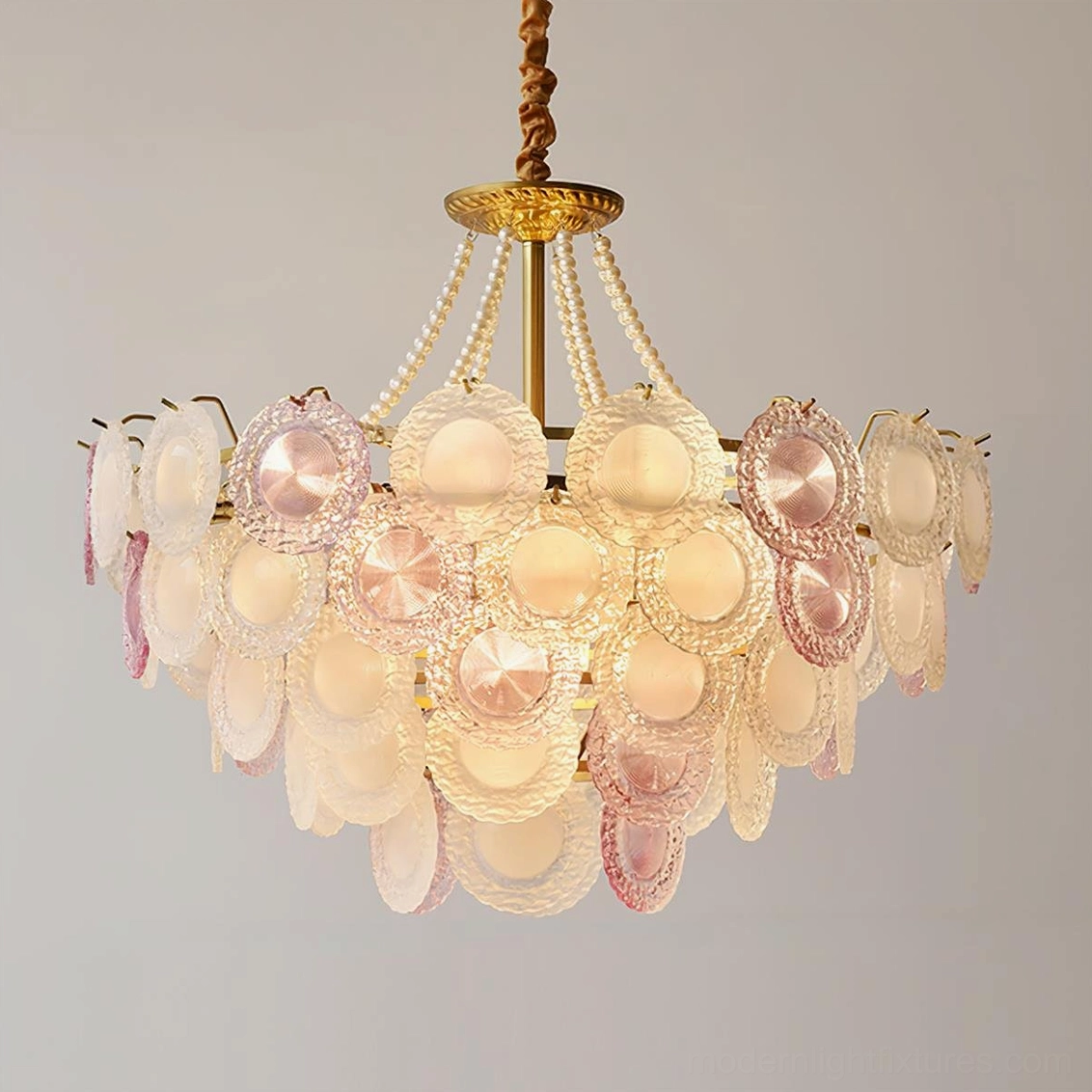 Violaire pink glass chandelier lit three-quarter view showing warm yellow light through frosted glass with pearl beaded chain