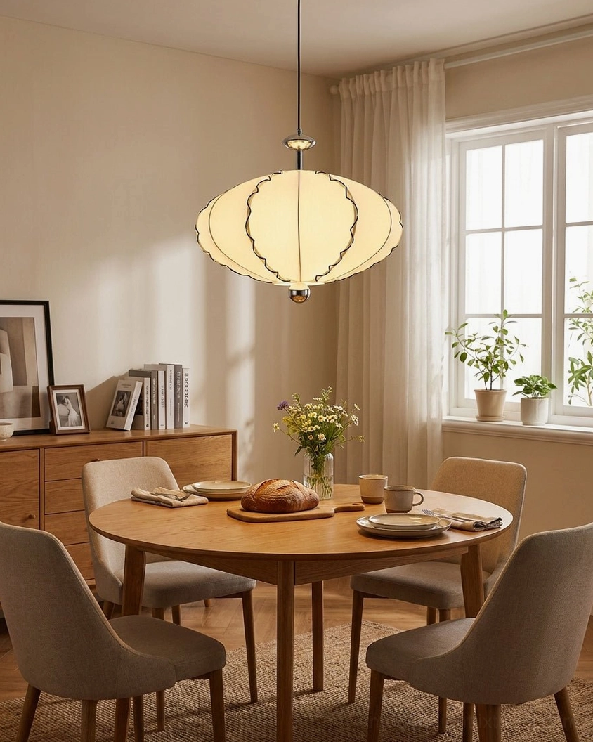 Modern cream pleated pendant light with warm white glow installed in minimalist dining room with walnut table and linen seating
