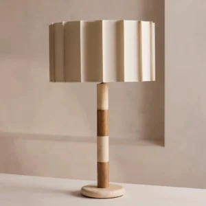 Modern pleated table lamp with cream fabric drum shade and segmented travertine stone and wooden stem, three-quarter angle