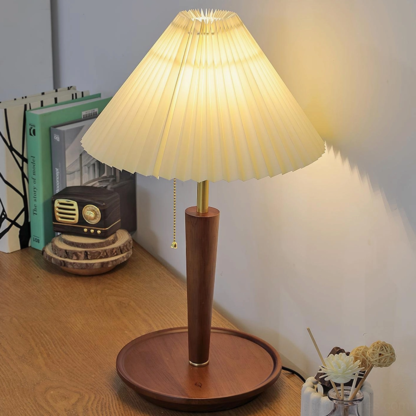 Contemporary pleated table lamp with solid wood base illuminating vintage radio and books on desktop, right angle view