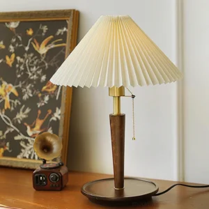 Mid-century modern pleated table lamp with gold hardware and pull-chain switch on wooden tabletop with vintage decor