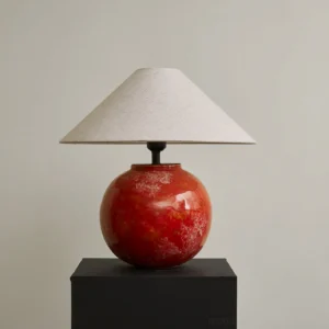 Contemporary red ceramic sculptural lamp with hand-finished glaze, displayed on black platform in minimalist interior setting
