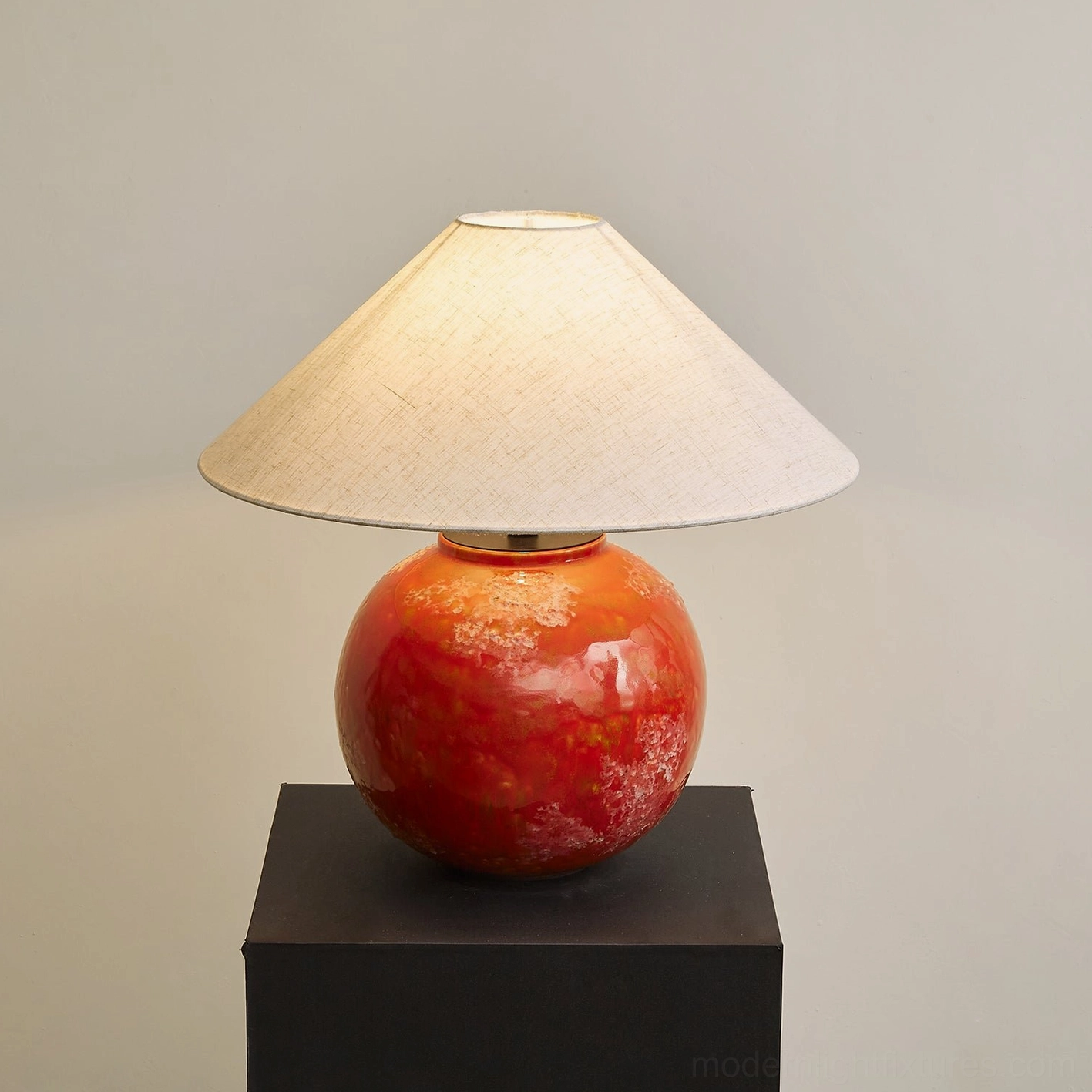 Contemporary red ceramic table lamp on black display plinth low angle three-quarter view with soft illuminated shade