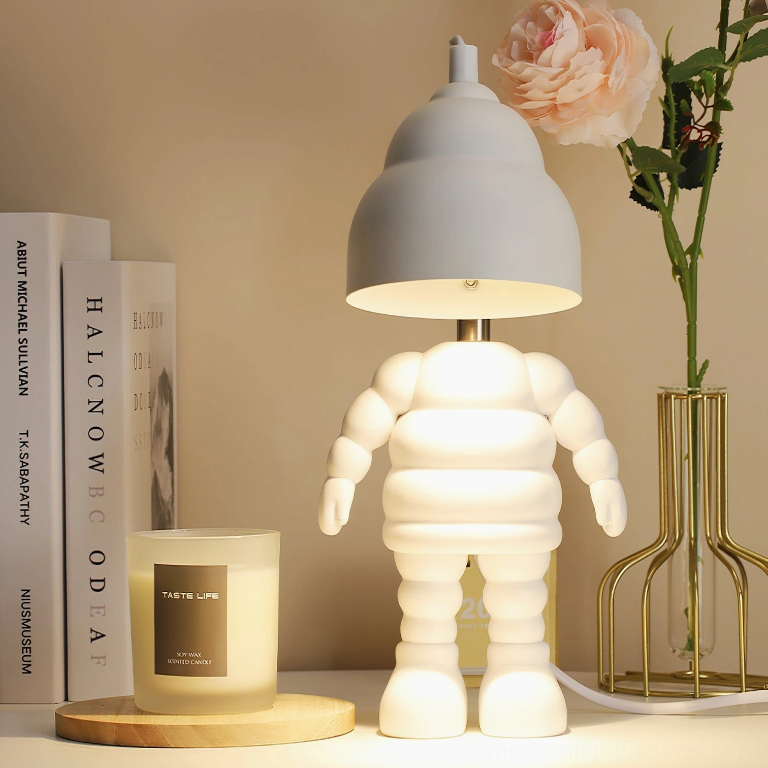 Sculptural robot candle warmer lamp with illuminated dome shade beside books and floral vase