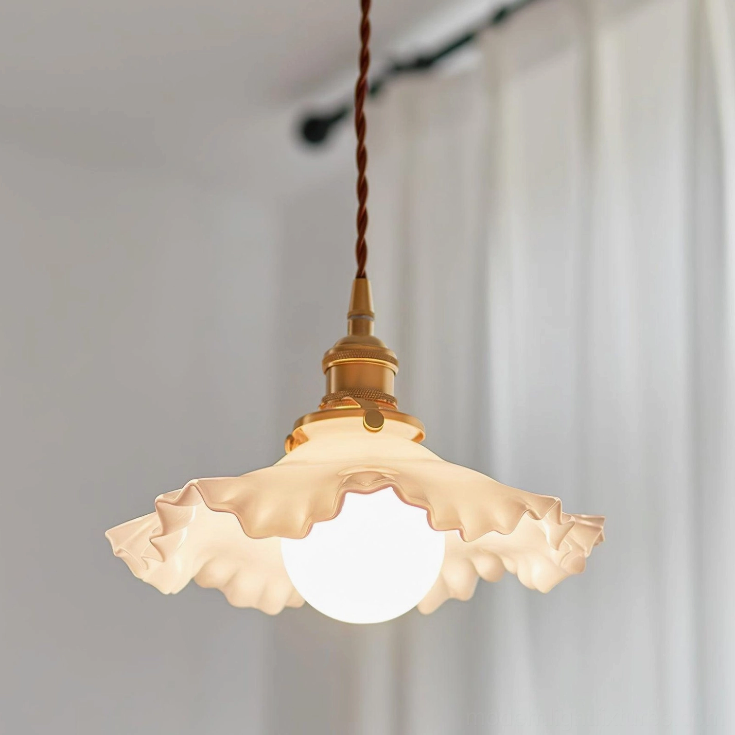 Ruffled pendant light fixture illuminated in soft warm glow, displayed hanging in modern interior space with sheer curtains