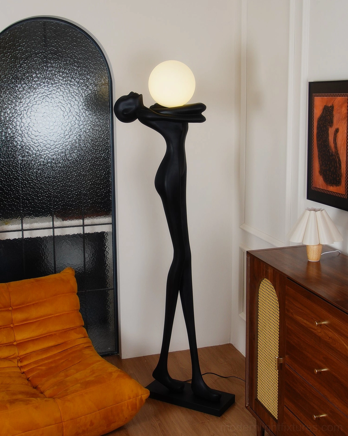 Abstract human figure floor lamp in contemporary bedroom, right three-quarter view with lit frosted glass shade