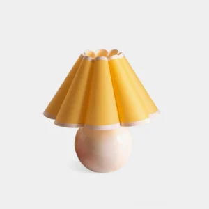 Modern sunburst pleated table lamp with white ceramic base and yellow fabric shade, front view on studio background