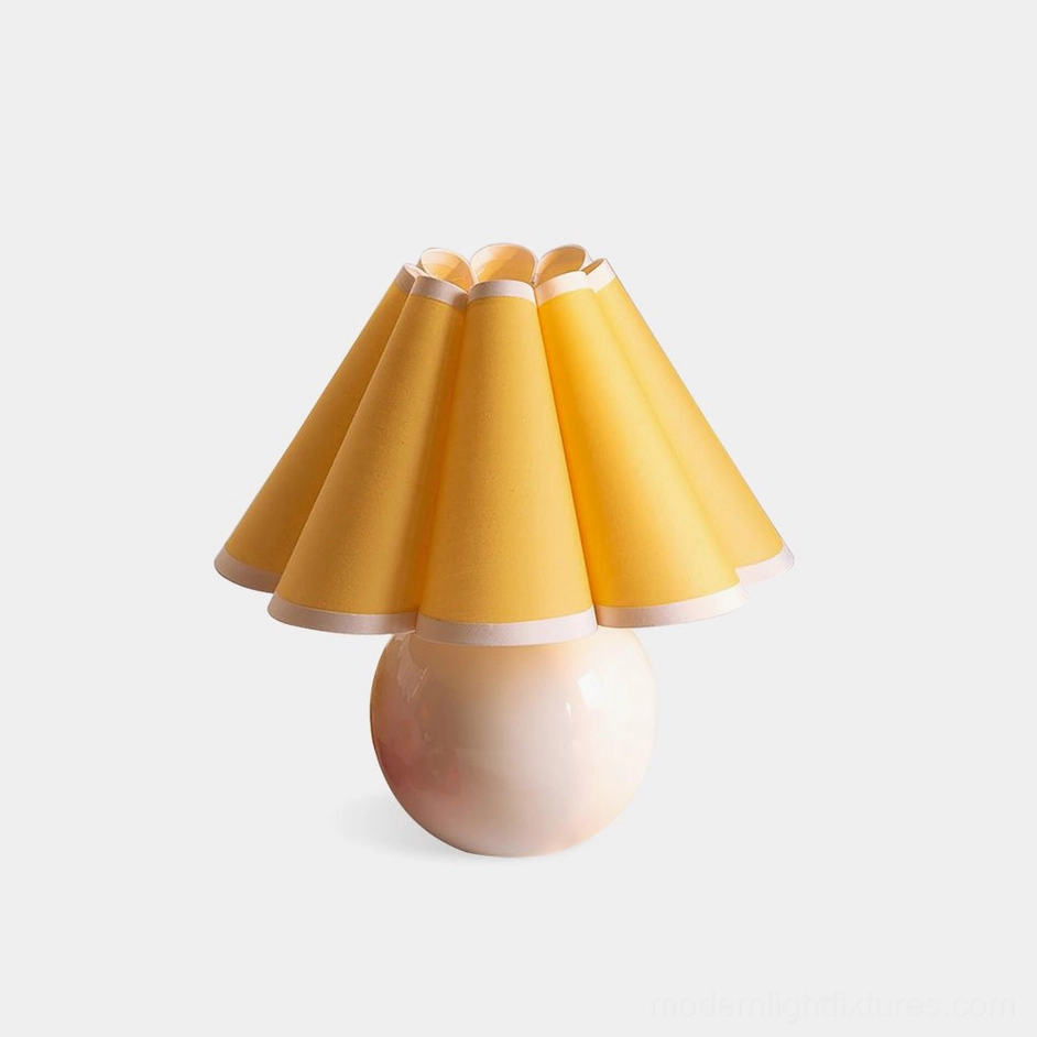 Modern sunburst pleated table lamp with white ceramic base and yellow fabric shade, front view on studio background