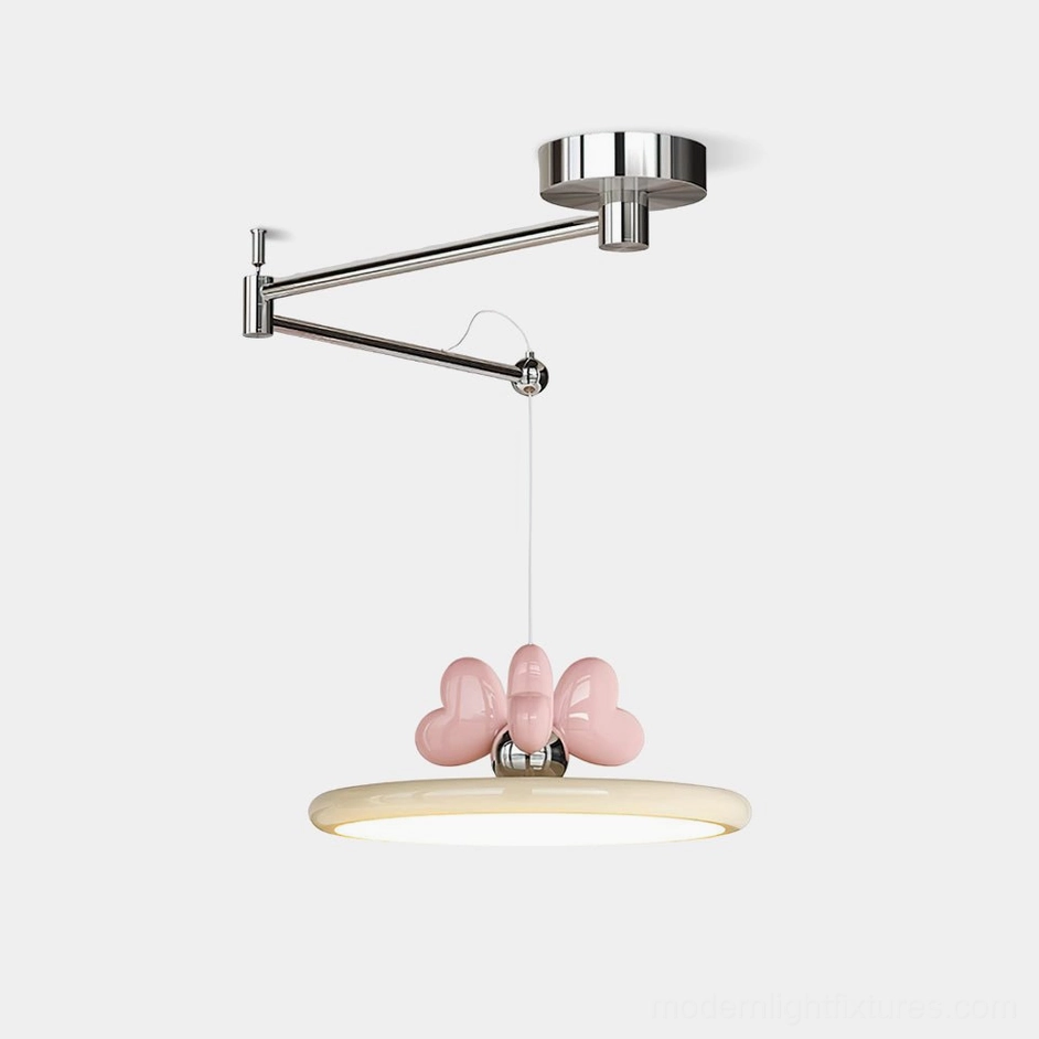 Modern swing arm pendant light with chrome metal arm, beige acrylic disc shade, and pink heart bow accent - front three-quarter studio view