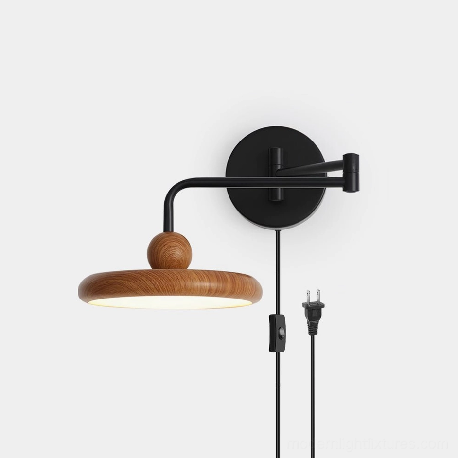 Modern swing arm wall sconce with adjustable matte black metal arm and warm wood-grain disc shade, front studio view