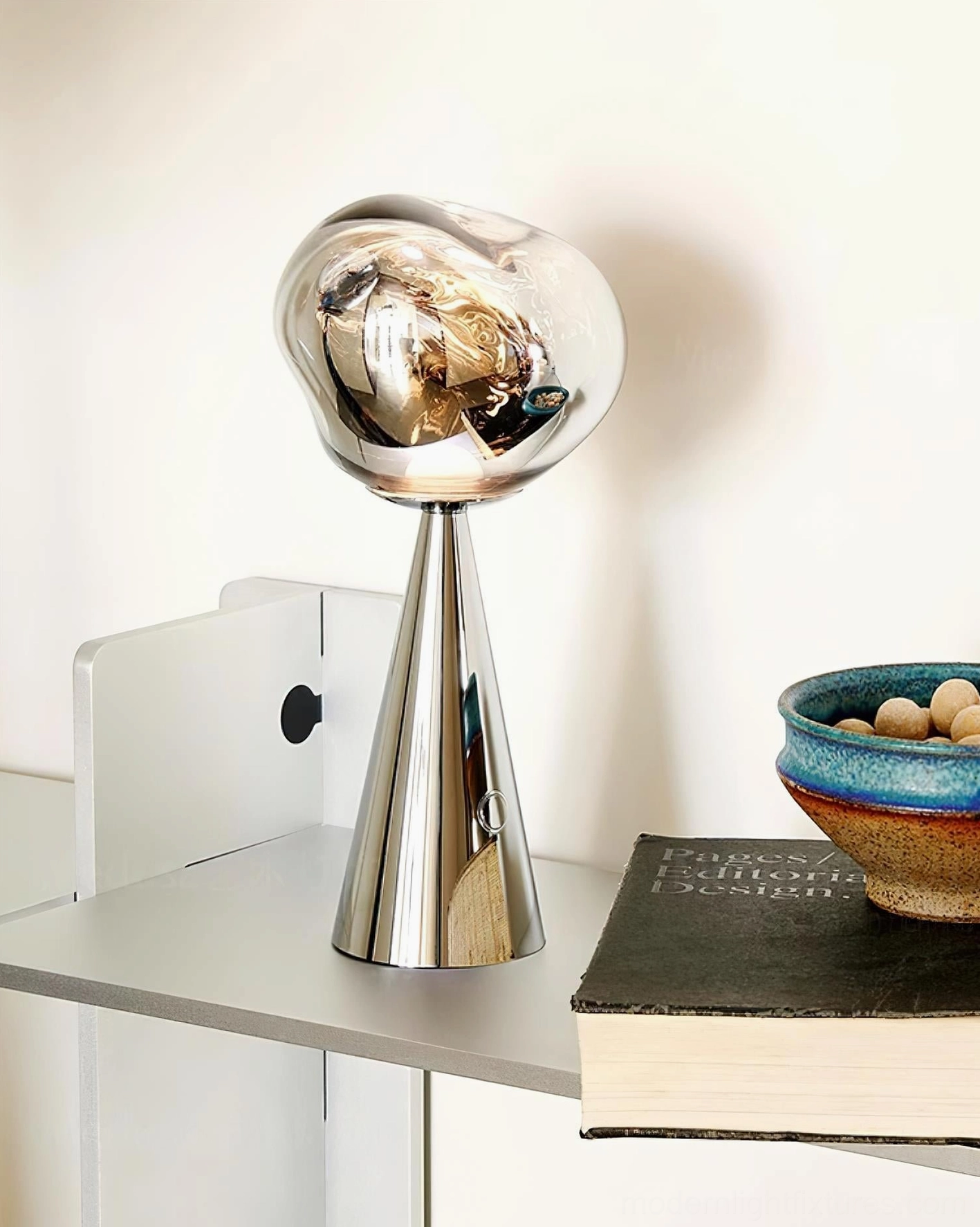 Modern silver table lamp unlit on floating shelf display, polished metal base with smoked glass shade, styled with book and ceramic