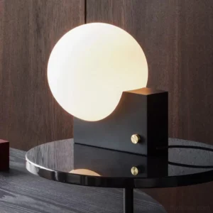 Modern minimalist table lamp with lit frosted glass globe, three-quarter angle showing warm glow effect