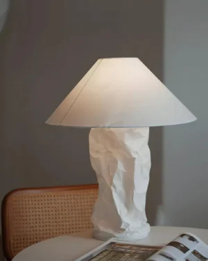 Contemporary table lamp displayed on side table with magazine and rattan chair in lifestyle setting