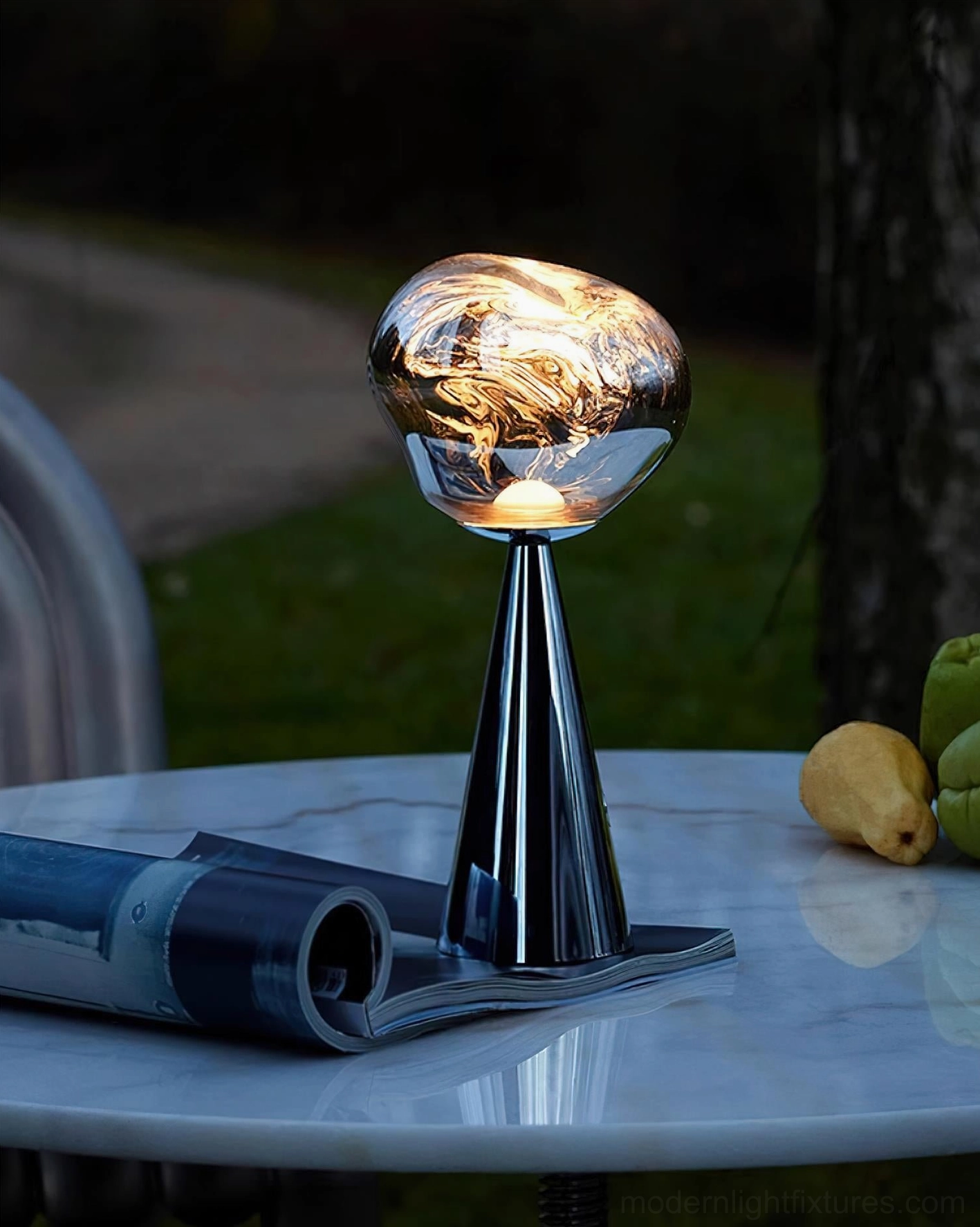 Outdoor modern table lamp on marble patio dining table, warm LED lighting for entertaining, three-quarter side view with garden decor
