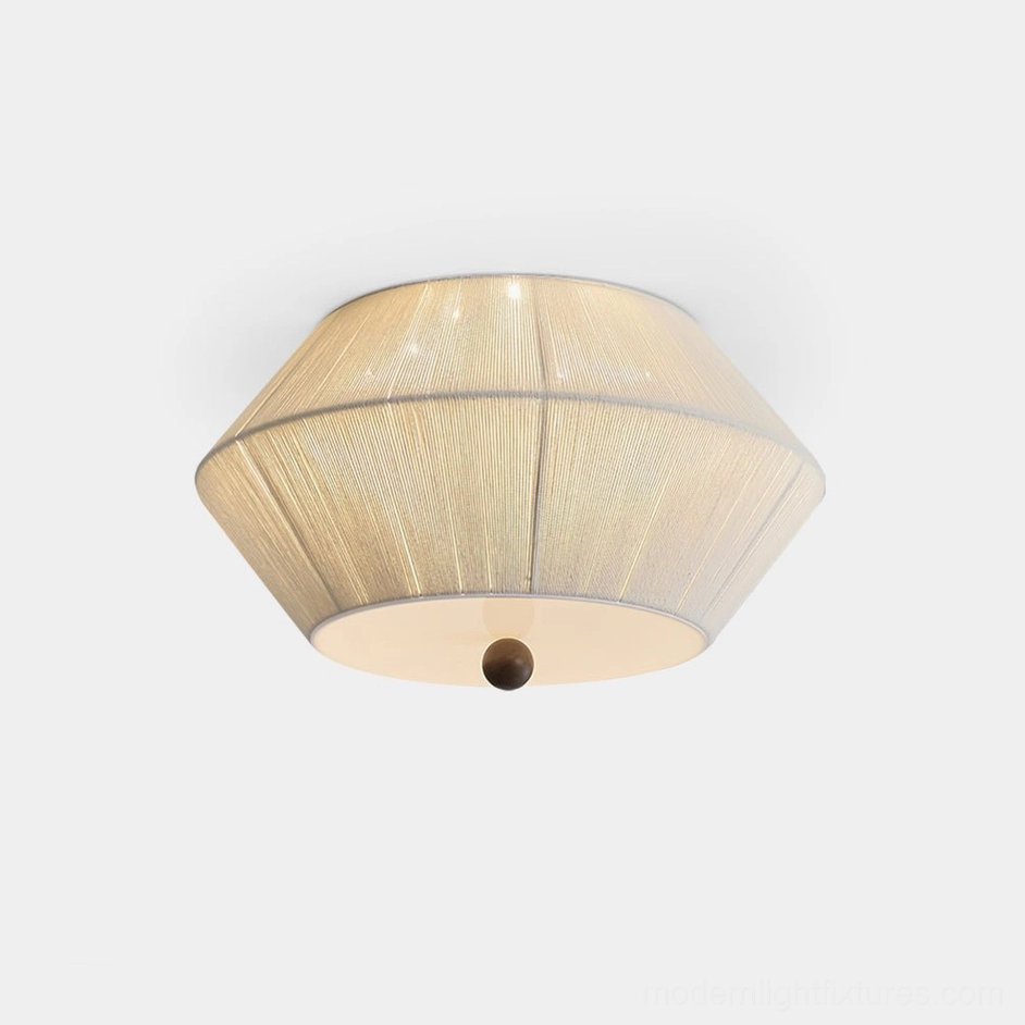Modern tapered fabric flush mount ceiling light with warm beige drum shade and dark spherical finial, studio overhead view