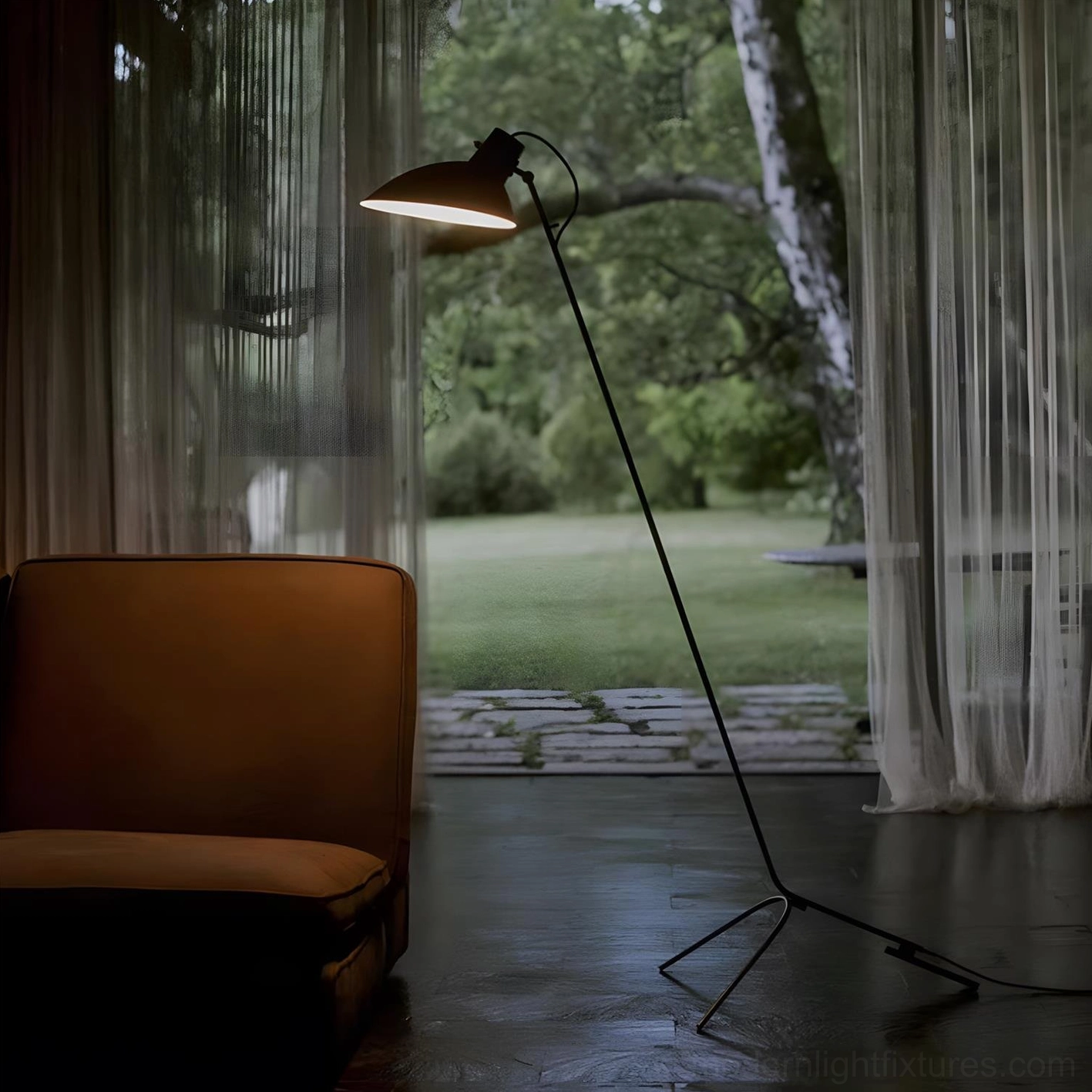 Black metal tripod floor lamp casting warm ambient light in contemporary living room with leather sofa and garden view