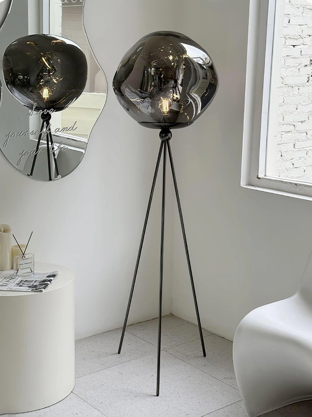 Modern tripod floor lamp with black metal stand and decorative smoked glass shade beside wooden display shelf