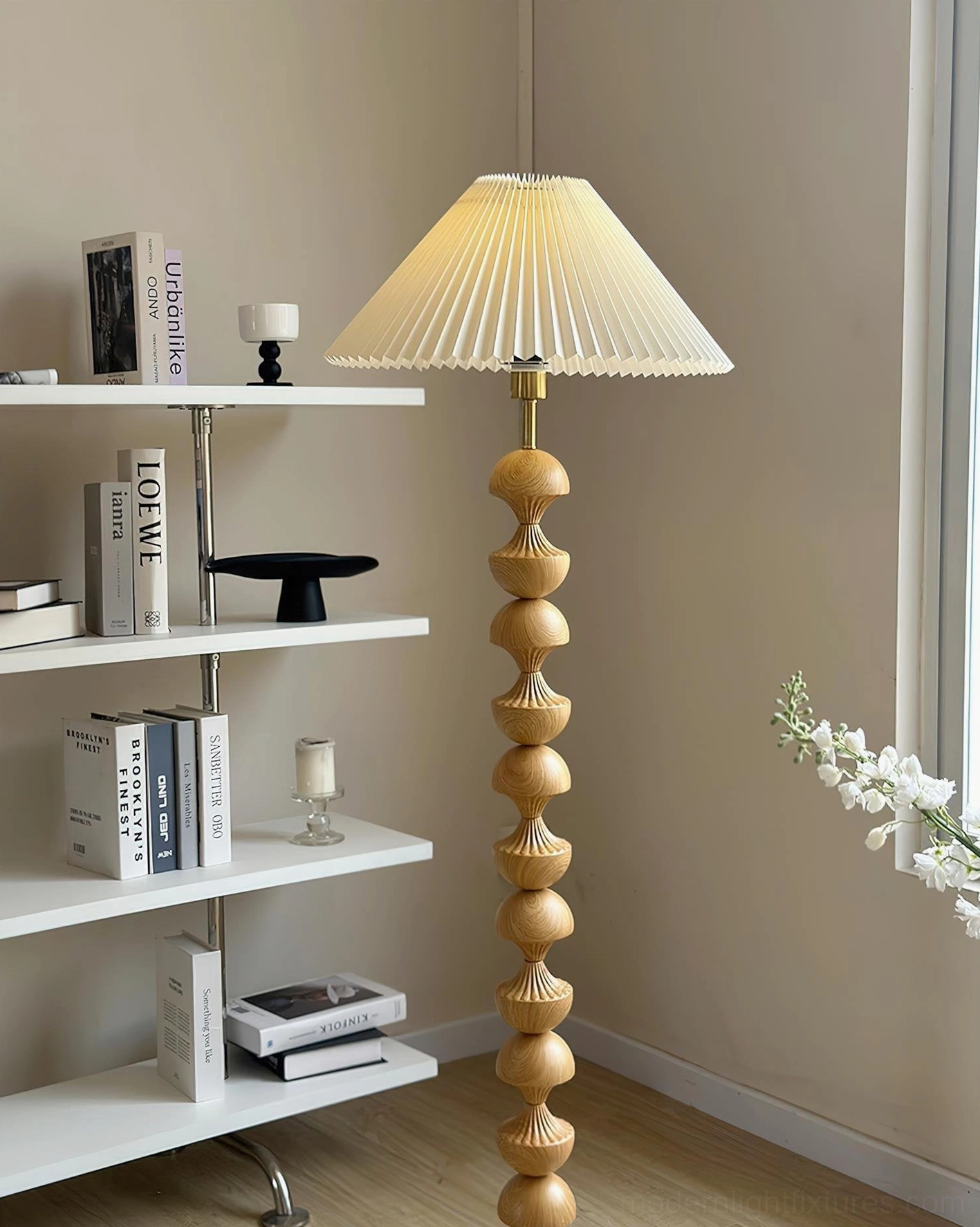 Pleated fabric shade wooden floor lamp three-quarter view in living room with white bookshelf decor, light wood grain sculptural pole, warm neutral aesthetic