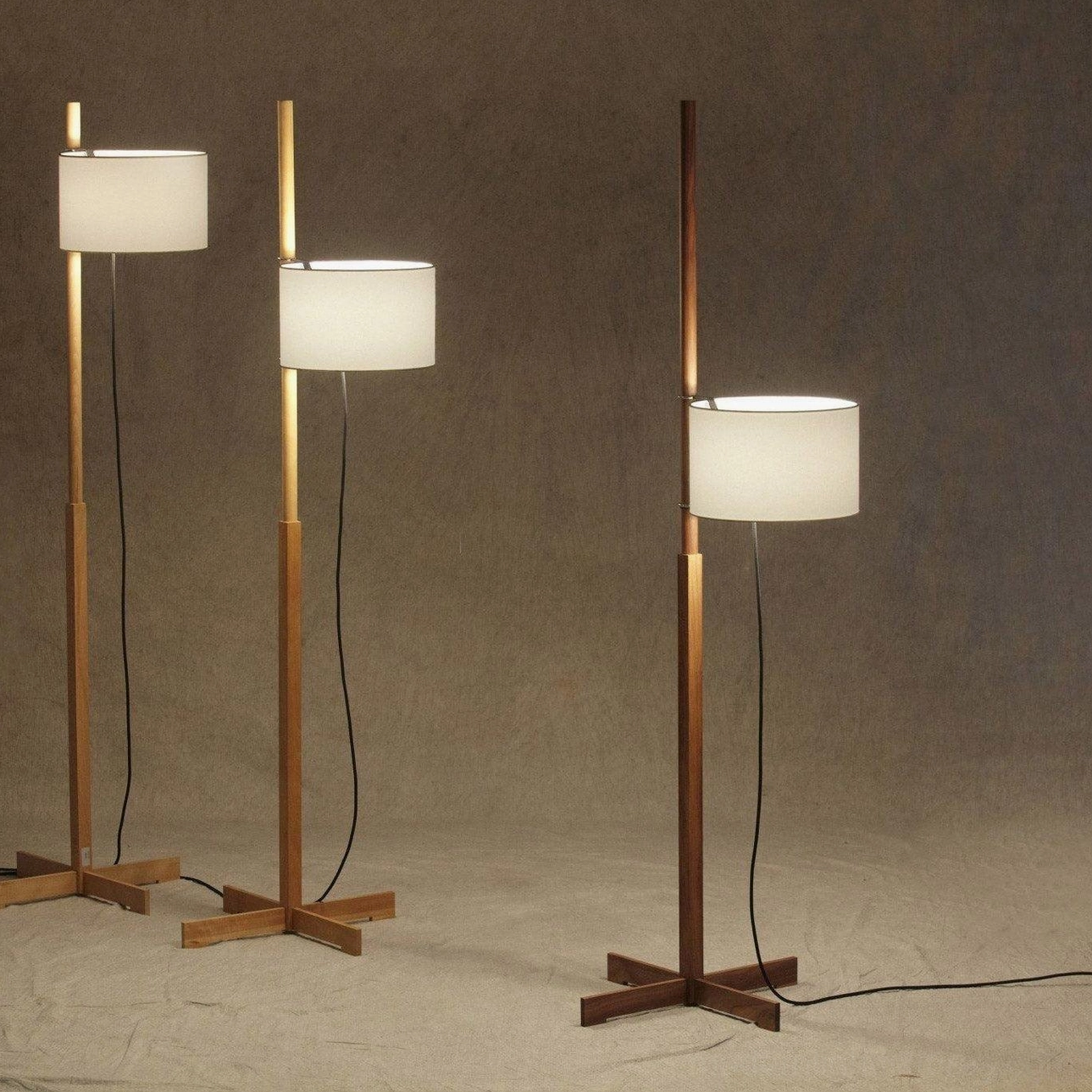 Set of three matching wooden floor lamps with white drum shades, neutral studio background
