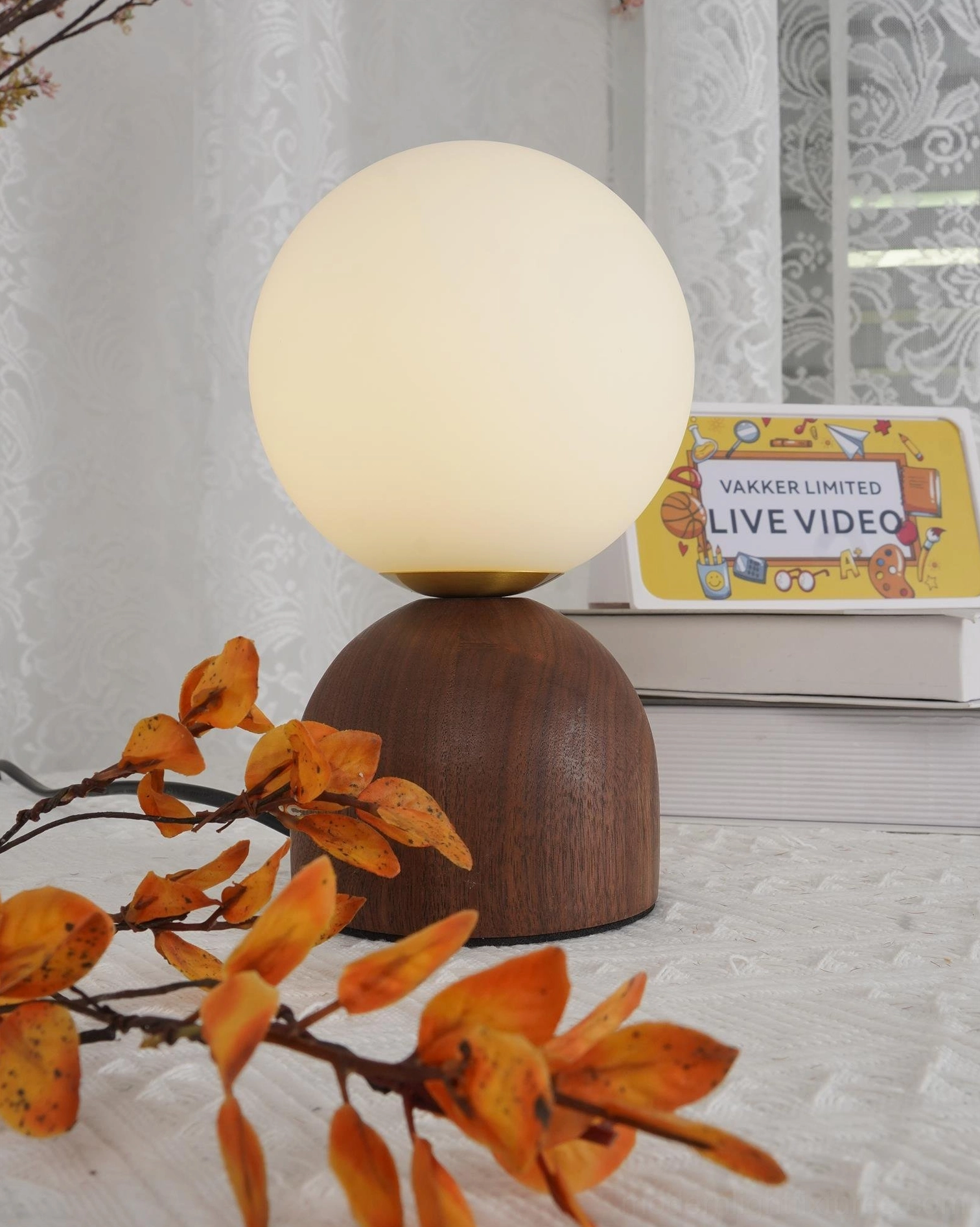 Frosted glass globe table lamp placed on textured tabletop with autumn foliage and books, warm ambiance