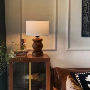 White wood table lamp placed on glass sideboard in living room with green plant decor - eye level interior shot