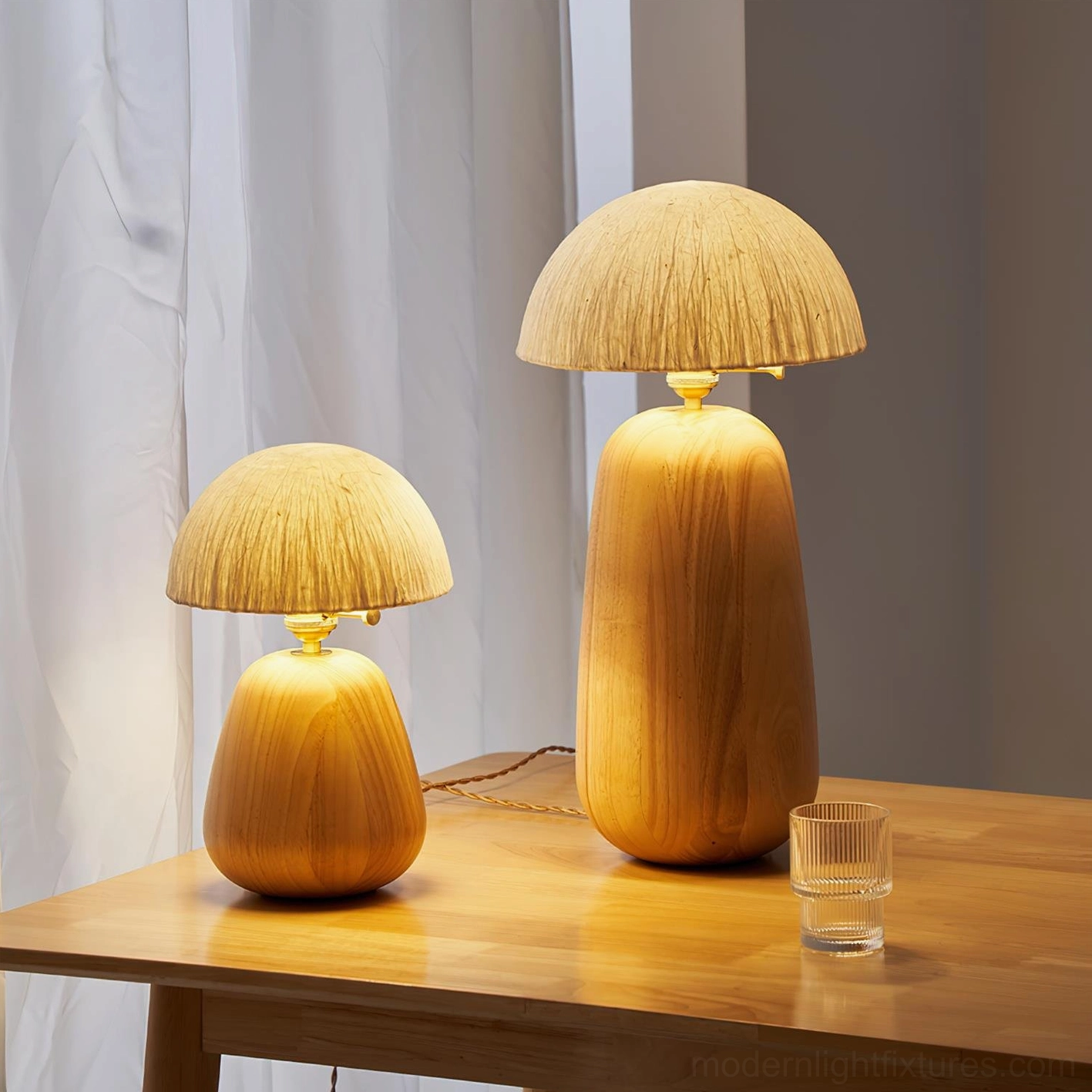 Two matching oak wood table lamps on tabletop with sheer curtain backdrop and clear glass decoration