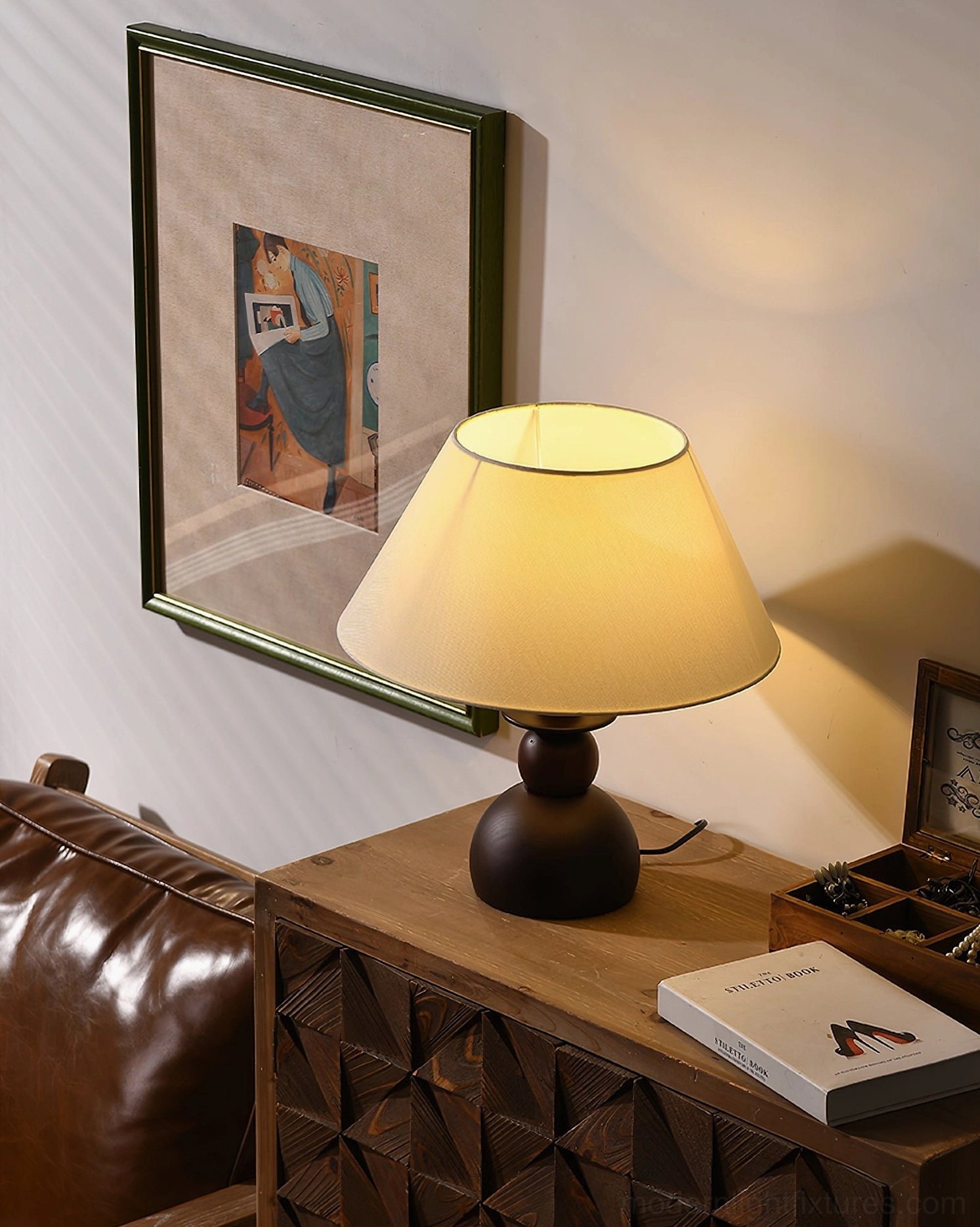 Walnut stacked wood table lamp beside leather sofa with decorative accessories and warm lighting