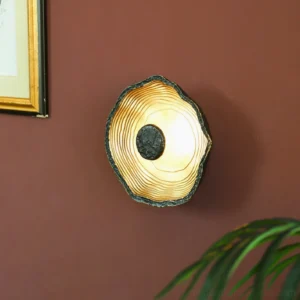 Modern black and brass wall sconce mounted on red wall with warm glowing light, artistic home gallery display with wabi-sabi aesthetic