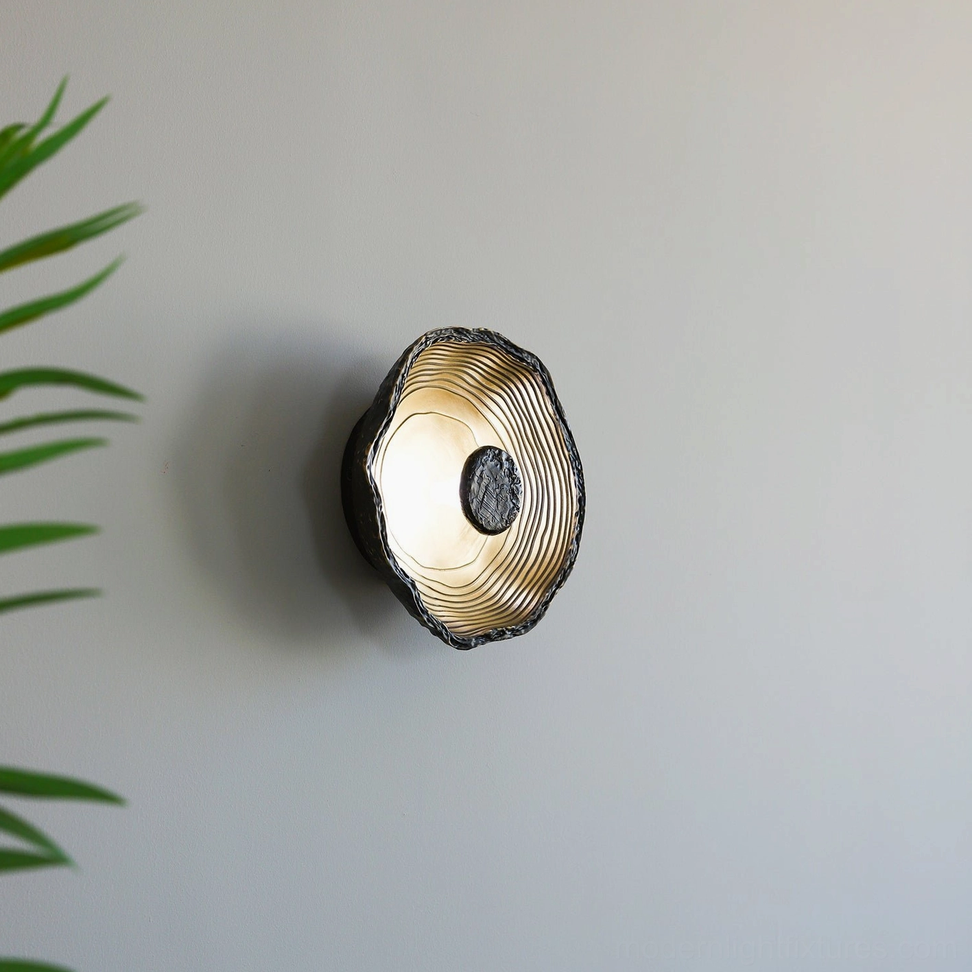 Moltena hand-formed wall sconce creating sculptural shadow play on wall, artistic lighting feature with distressed black exterior
