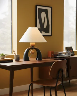 Modern arch table lamp positioned on home office desk with mustard accent wall and wooden furniture setup