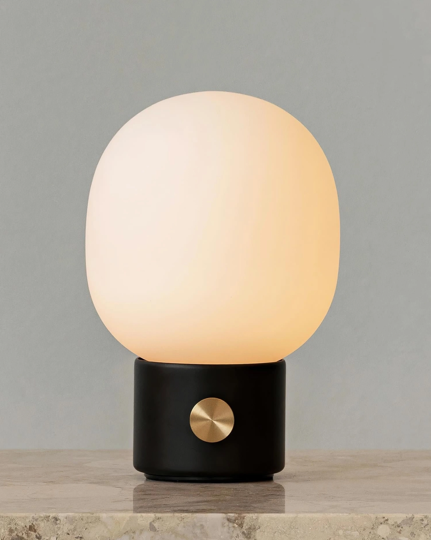 Black Monolith table lamp close-up with frosted glass shade emitting warm glow on stone surface