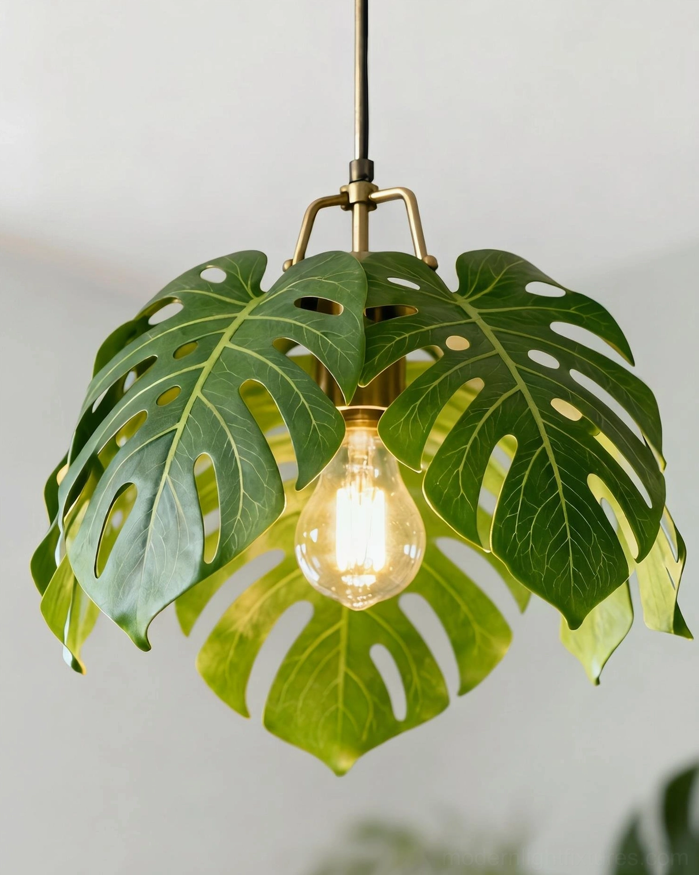 Monstera leaf pendant light close-up showing layered resin leaves with exposed bulb socket and polished brass hardware